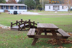 Una mesa de picnic con banco de madera y un pequeño puente en un césped.