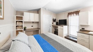 Ein kleines Zimmer mit Bett, Schreibtisch, Küchenzeile und Fernseher.