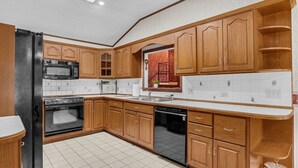Une cuisine avec des meubles de rangement en bois, un réfrigérateur noir, un four à micro-ondes, un four traditionnel et un lave-vaisselle.