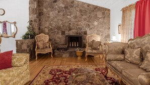 Un salon avec une cheminée en pierre, deux fauteuils décoratifs, un canapé et un tapis rouge à motifs.