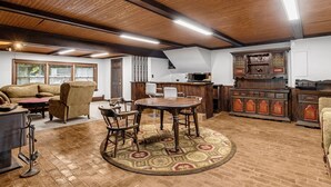 Un salon chaleureux avec un plafond en bois, une table ronde entourée de chaises, un canapé et un tapis à motifs.