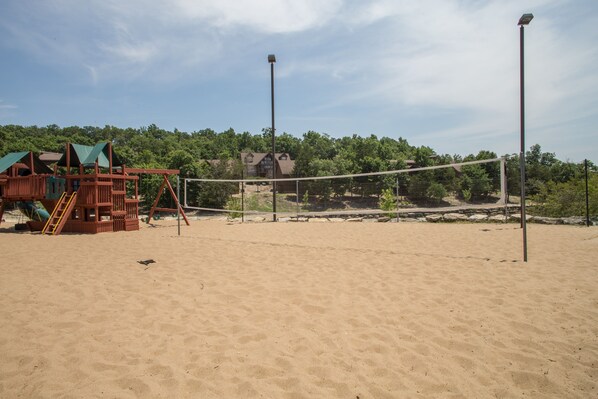 Una playa arenosa con una red de voleibol, una estructura de juego de madera y un edificio al fondo.