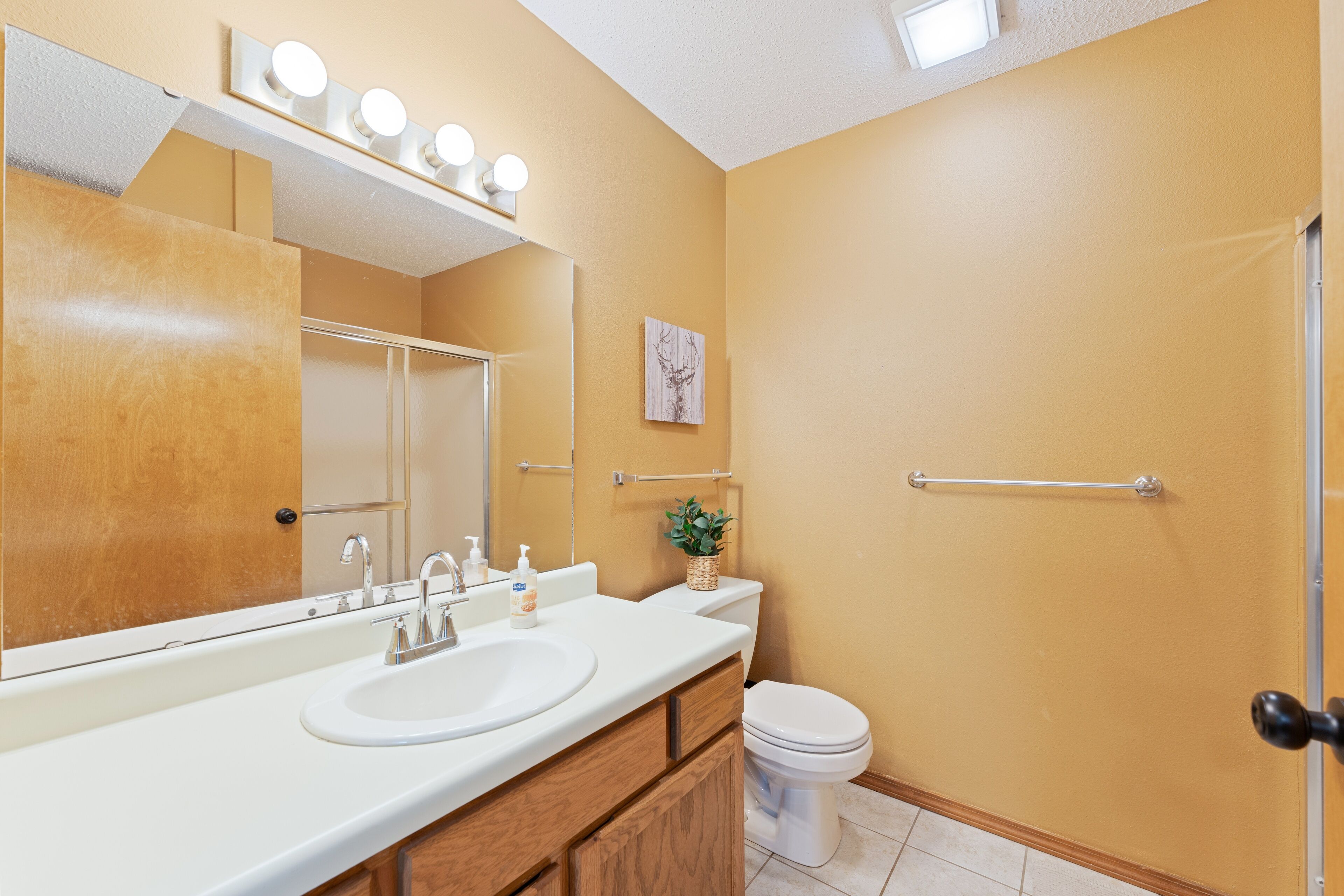 A bathroom with a sink, mirror, and toilet. There are lights above the mirror and a towel rack.