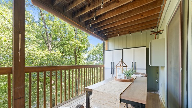 Une terrasse en bois avec une table et des chaises, un luminaire suspendu et une vue sur les arbres.