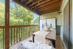 A wooden deck with a table and chairs, a hanging light fixture, and a view of trees. - Ne16-2 Sleepy Bear Camp 2 Bedroom Condo (Branson West)
