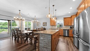 Une cuisine spacieuse avec des meubles en bois, un grand îlot central, des appareils électroménagers en acier inoxydable et un éclairage suspendu.