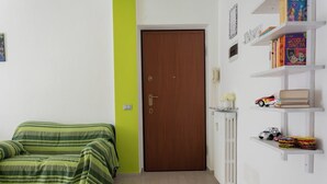 A room with a green-striped sofa, a wooden door, and a white wall with shelves holding books and toys. - Zona Fiera Rho Però, IRCCS Ospedale Galeazzi - Sant'Ambrogio for families  (Rho)