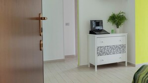 A bedroom with a bed, a TV mounted on the wall, a small white bedside table with a plant, and a door leading to another room. - Zona Fiera Rho Però, IRCCS Ospedale Galeazzi - Sant'Ambrogio for families  (Rho)