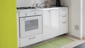 A modern kitchen with white cabinets, a gas stove, a coffee maker, and a tiled backsplash. - Zona Fiera Rho Però, IRCCS Ospedale Galeazzi - Sant'Ambrogio for families  (Rho)