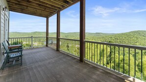 Una terraza de madera con barandilla, un banco y vistas a colinas verdes.