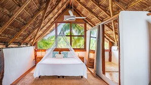 Une chambre avec un lit, un ventilateur de plafond et une grande fenêtre donnant sur des palmiers.
