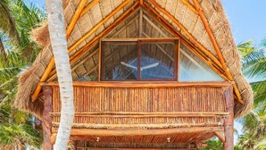 Un bungalow au toit de chaume, doté d’une terrasse en bois, de grandes fenêtres et offrant une vue sur les palmiers.