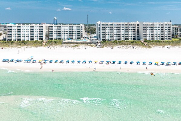 A beachfront hotel with multiple floors, a sandy beach, and a row of umbrellas. - Beach House 304b 1 Bedroom Condo (Miramar Beach)