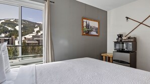 A hotel room with a bed, a window with a view of a mountain, a small table with a coffee maker, and a framed picture on the wall.