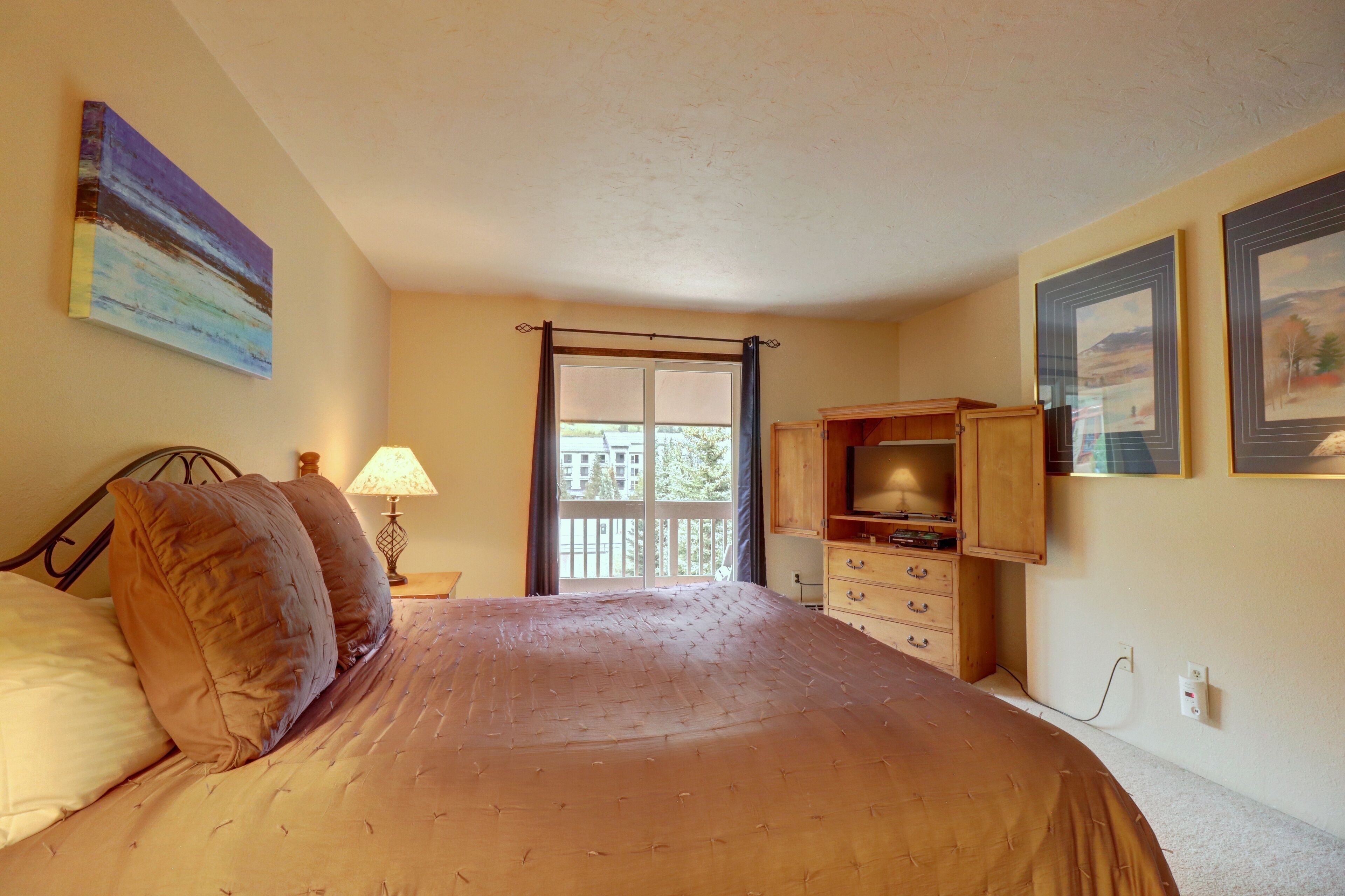 Quarto com cama, penteadeira, televisão e janela com vista para o exterior.