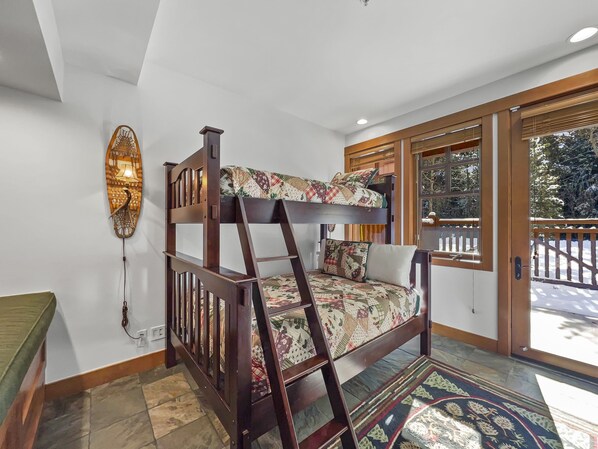 Habitación con literas, una escalera de madera, una colcha estampada y un adorno de pared.