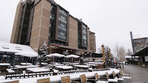 Ein mit Schnee bedeckter Außenbereich mit Tischen und Stühlen, ein Gebäude mit großen Fenstern und ein Schild mit der Aufschrift "Ten Mile".