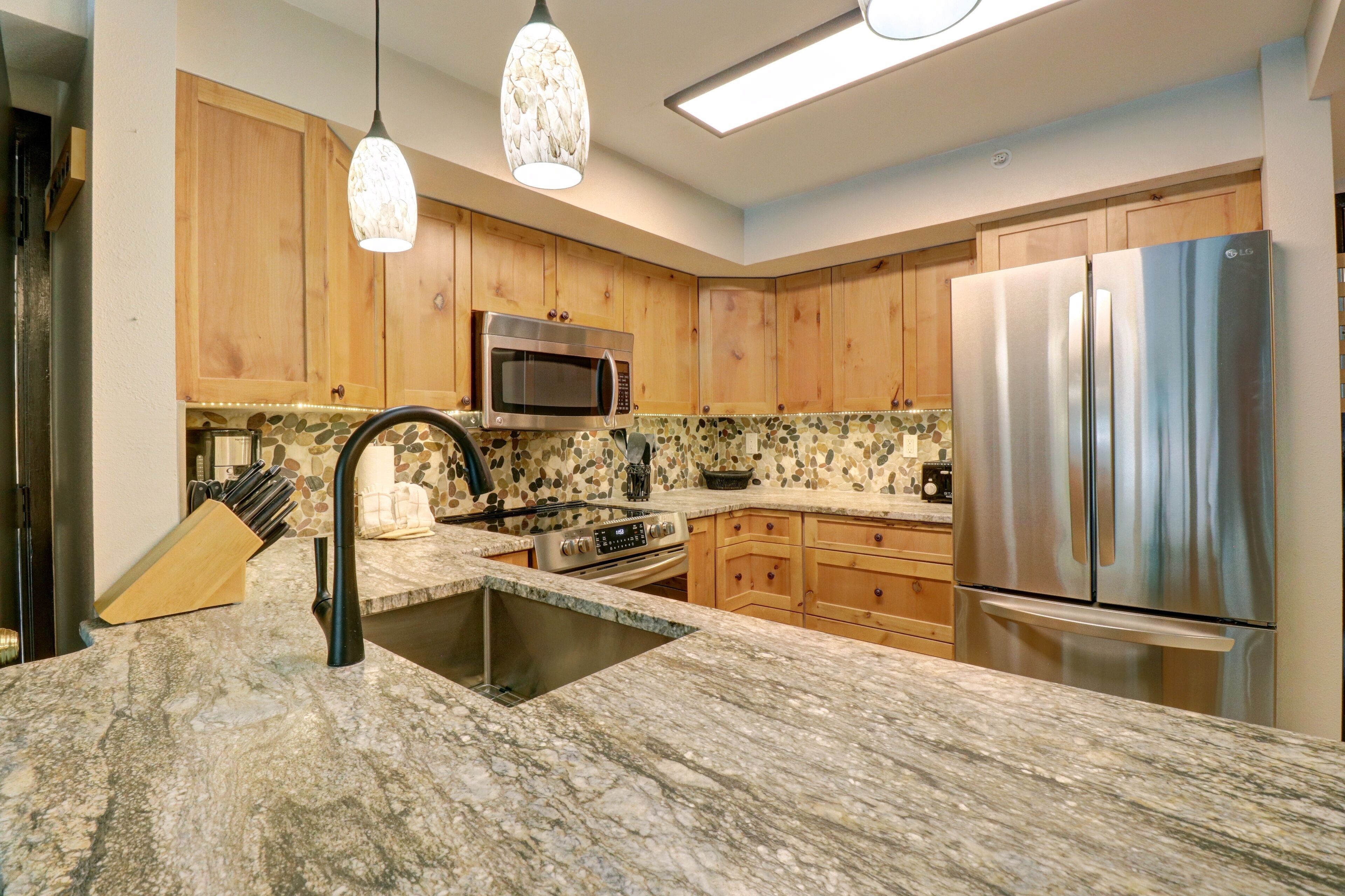 A kitchen with wooden cabinets, a stainless steel refrigerator, a microwave, and a granite countertop.