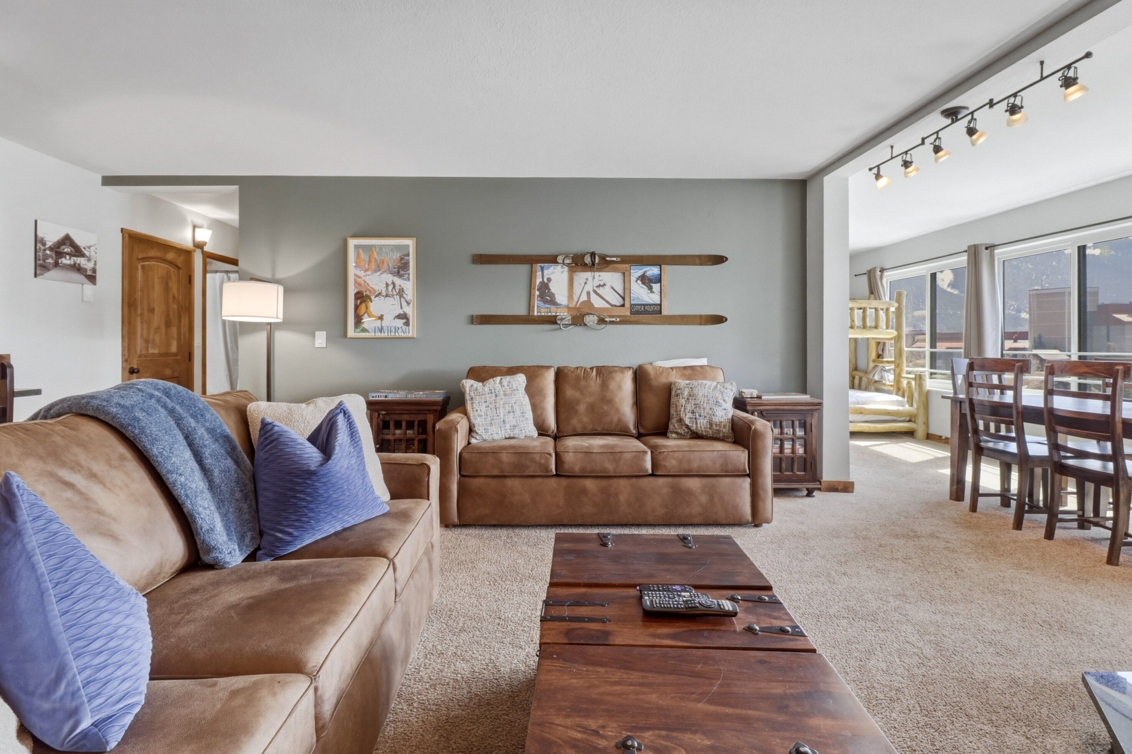 A spacious living room with a brown leather sofa, a wooden coffee table, and a dining area with wooden chairs and a table.