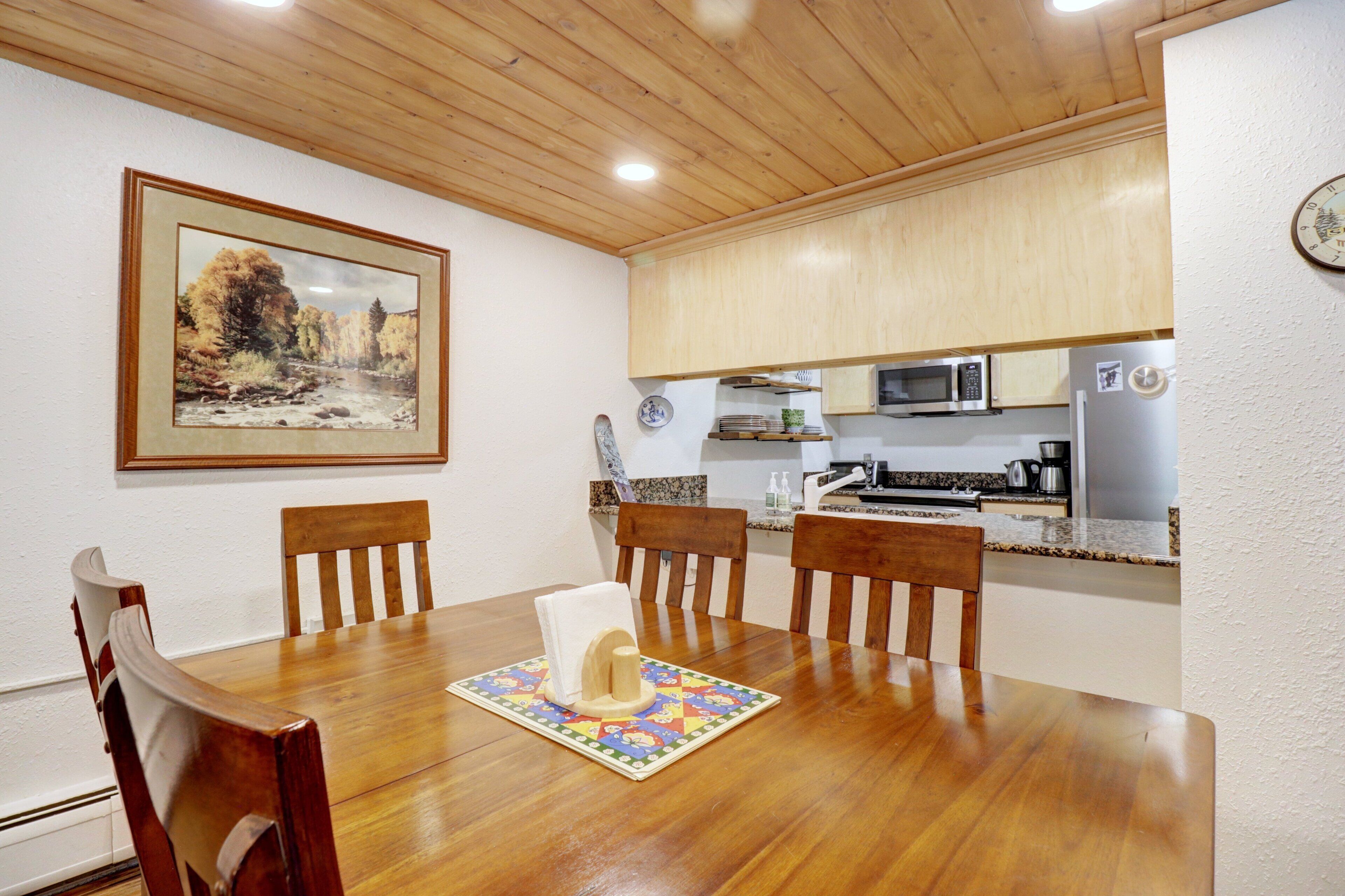 A dining area with a wooden table, chairs, and a framed landscape painting on the wall.
