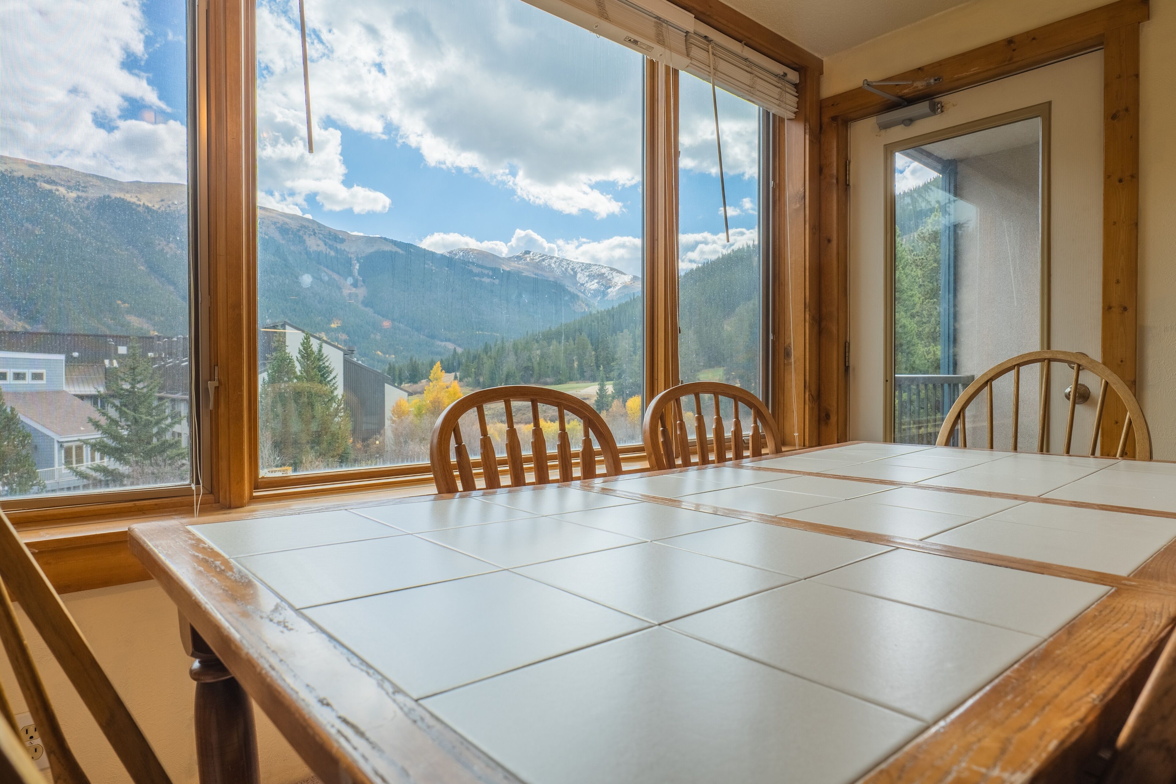A dining area with a large table and chairs, large windows with a mountain view, and wooden walls.