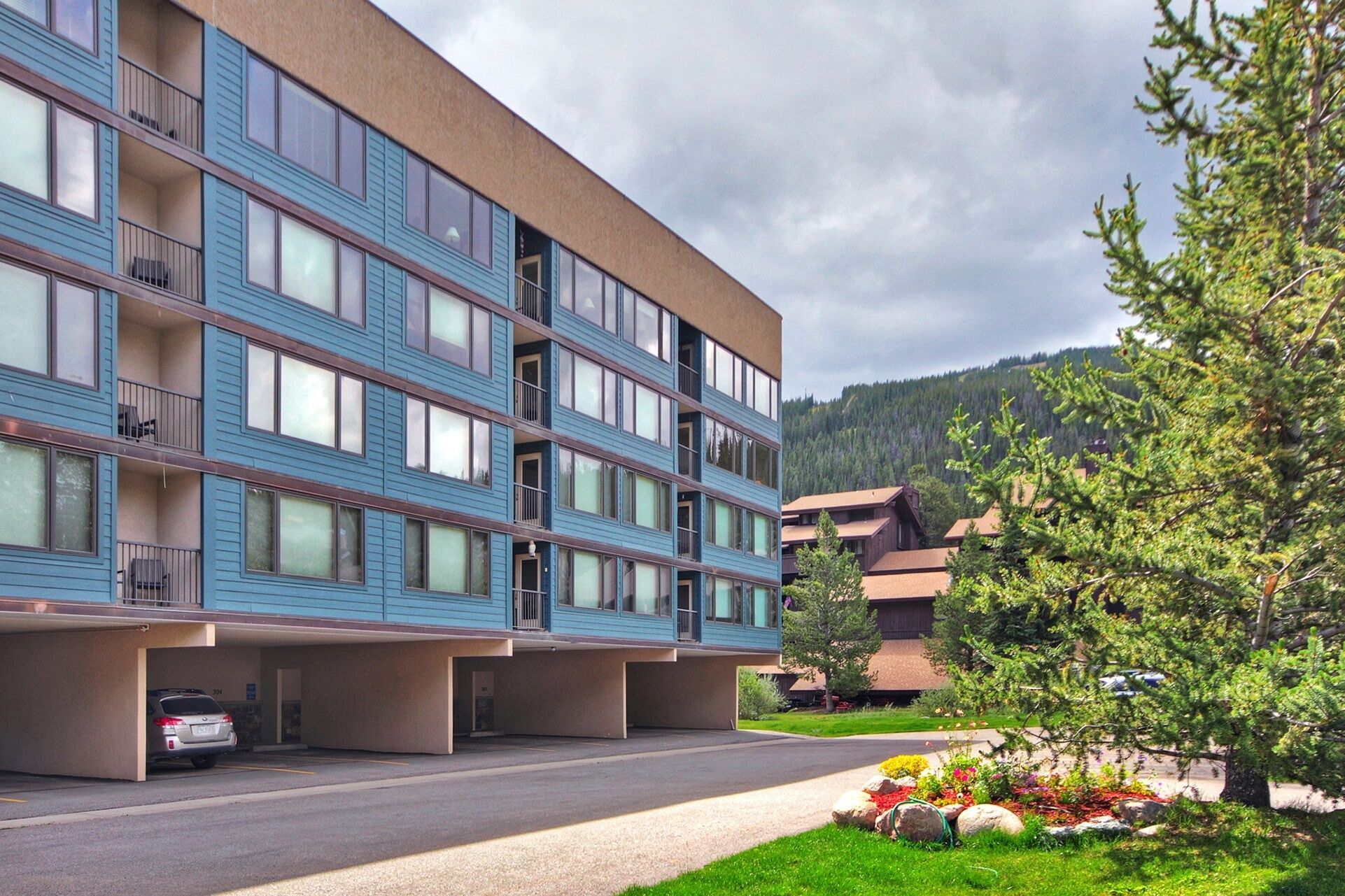 A multi-story hotel with a blue facade, balconies, and a parking area.