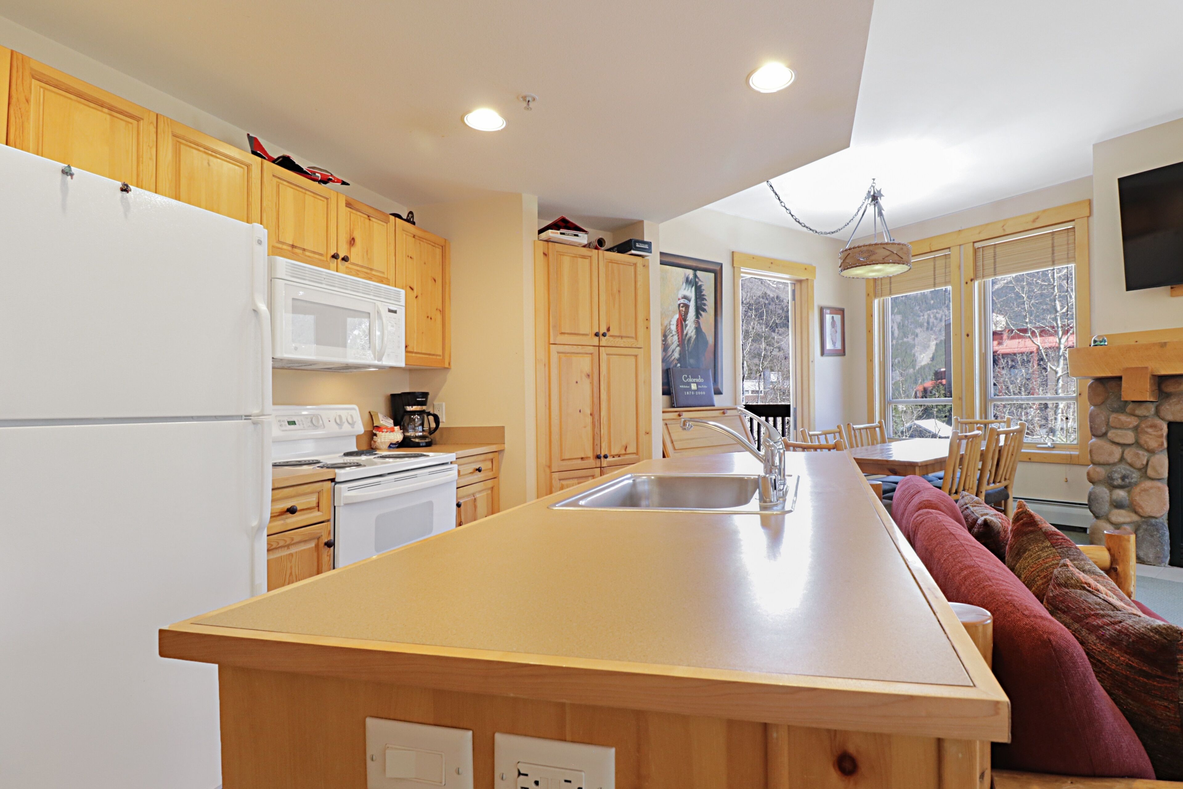 A kitchen with wooden cabinets, a white refrigerator, a microwave, a stove, and a large island with a sink.