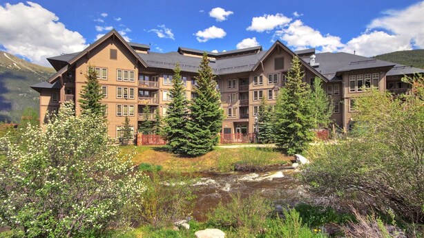 A multi-story hotel with balconies, surrounded by natural scenery and a small stream. - Tx314 Taylors Crossing 2 Bedroom Condo (Copper Mountain)