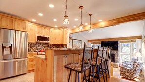 A spacious kitchen with wooden cabinets, a large island with bar stools, stainless steel appliances, and a stone backsplash.