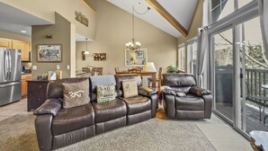 A spacious living room with a brown leather sectional sofa, a dining area with a wooden table and chairs, and a large sliding glass door leading to an outdoor deck. - B6 Tarn Landing 1br + Loft, 3ba 1 Bedroom Condo (Frisco)