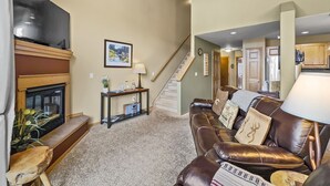 A living room with a fireplace, leather sofa, and a staircase leading to another level. - B6 Tarn Landing 1br + Loft, 3ba 1 Bedroom Condo (Frisco)