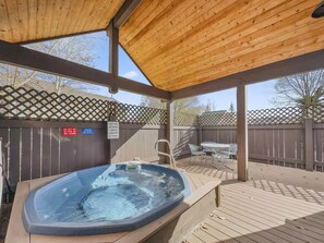 A hot tub under a wooden pergola with a wooden fence and a sign indicating hot tub usage rules.