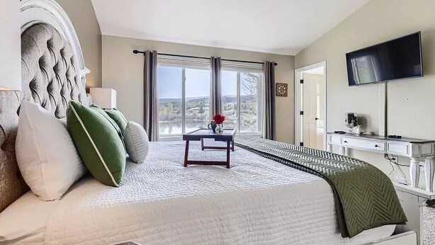 A bedroom with a large bed, a desk, a television, and a window with a view.