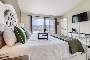 Un dormitorio con una cama grande, un escritorio, un televisor y una ventana con vistas.