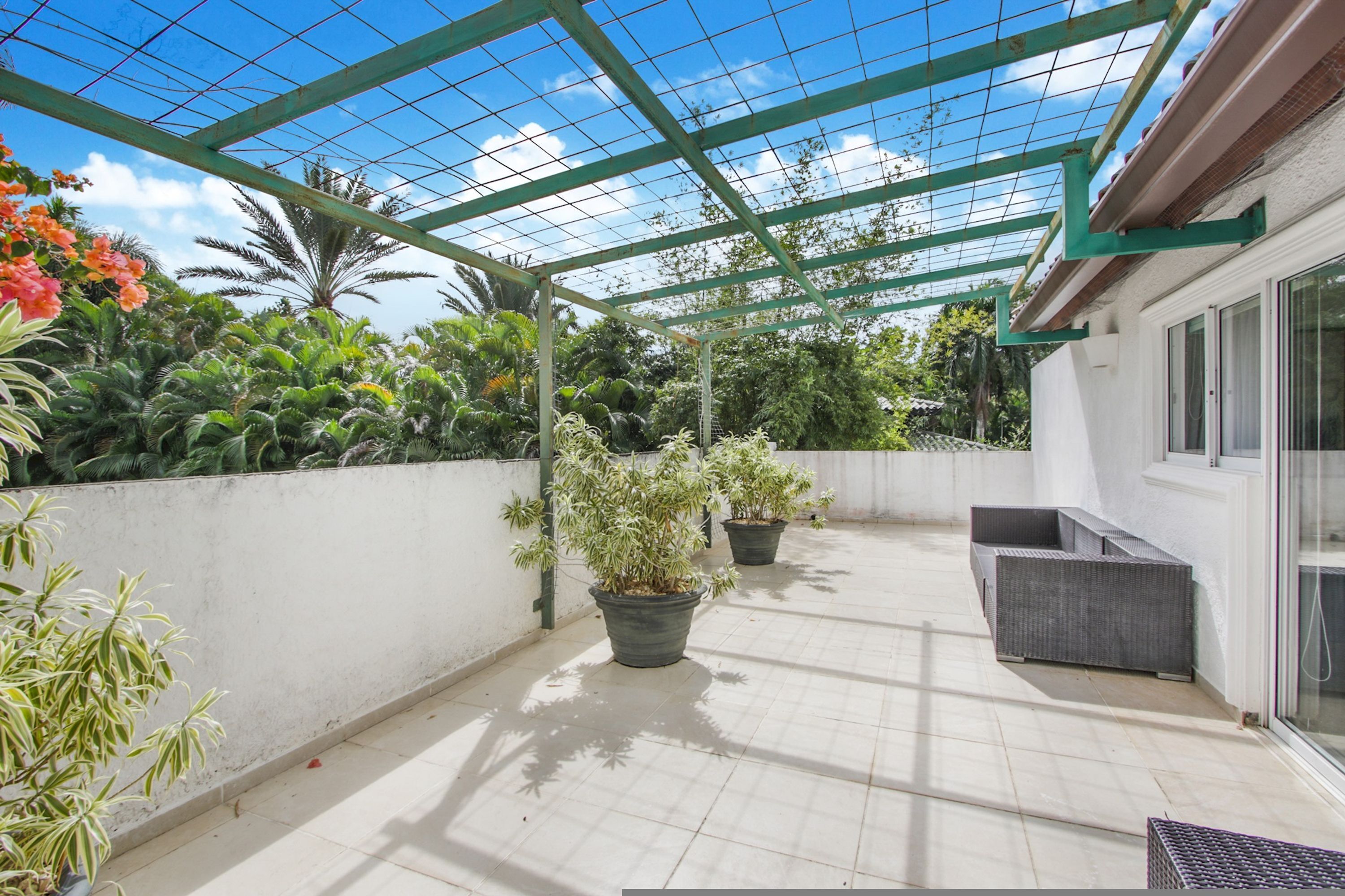 Un patio couvert agrémenté de plantes en pot, de meubles d’extérieur et offrant une vue dégagée sur le ciel.