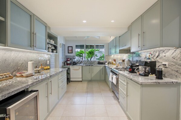A modern kitchen with marble countertops, built-in appliances, and a view of greenery outside.