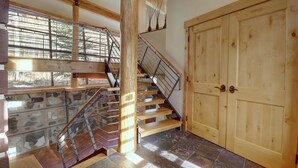 Eine Holztreppe mit Metallgeländern, einem Steinplattenboden und einer großen Holztür.