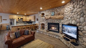Un salón acogedor con chimenea de piedra, un sofá de cuero y una cocina al fondo.