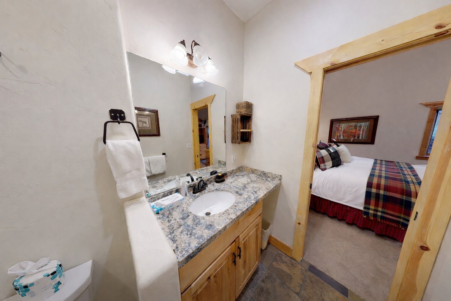 A bathroom with a granite sink, a mirror, a towel rack, and a wooden cabinet.