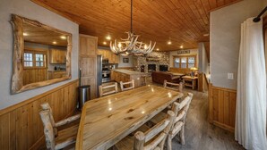 Un interior rústico con una mesa de comedor de madera, sillas, una araña y una chimenea de piedra.