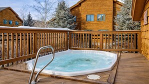 Una terraza de madera con un jacuzzi y una casa de madera al fondo.