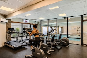 Ein Fitnessstudio mit Laufbändern, Crosstrainern und einem Pool, der durch eine Glaswand sichtbar ist.