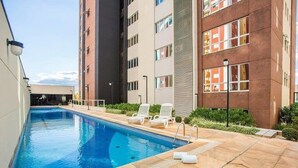 A swimming pool area with a clear blue pool, white lounge chairs, and a modern building with multiple floors and large windows. - Premium Suite No. 102 at the Metropolitan Hotel in Bauru, with magnificent breakfast (Jardim Estoril Bauru)