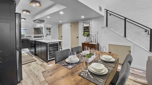 A modern kitchen with dark cabinetry, a central island, and a dining area set for six with a wooden table and grey chairs.