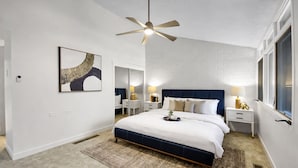 A bedroom with a bed, bedside tables, a ceiling fan, a wall-mounted artwork, and a window.