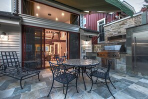 An outdoor patio with a round table and chairs, a grill, and a stone wall. - 521 Woodside Gem True Ski-in Ski-out On The Gold Coast 3 Bedroom Home (Park City)