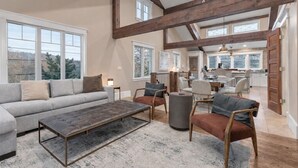 A spacious living room with a sofa, armchairs, and a coffee table. There are large windows providing natural light and a view of the outdoors. - 521 Woodside Gem True Ski-in Ski-out On The Gold Coast 3 Bedroom Home (Park City)