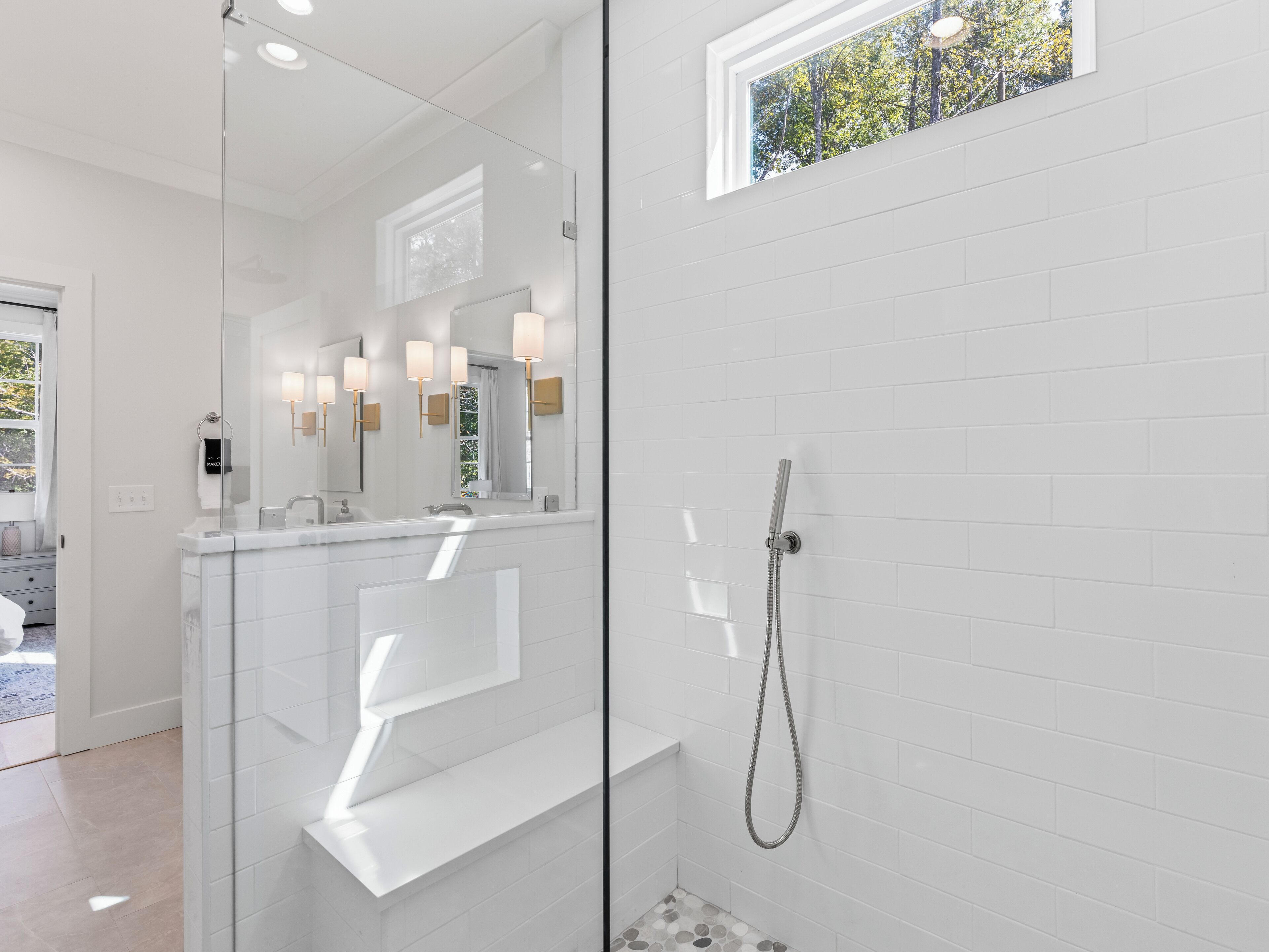 Een moderne badkamer met een douchecabine van glas, witte metro tegels en een raam met uitzicht op bomen.