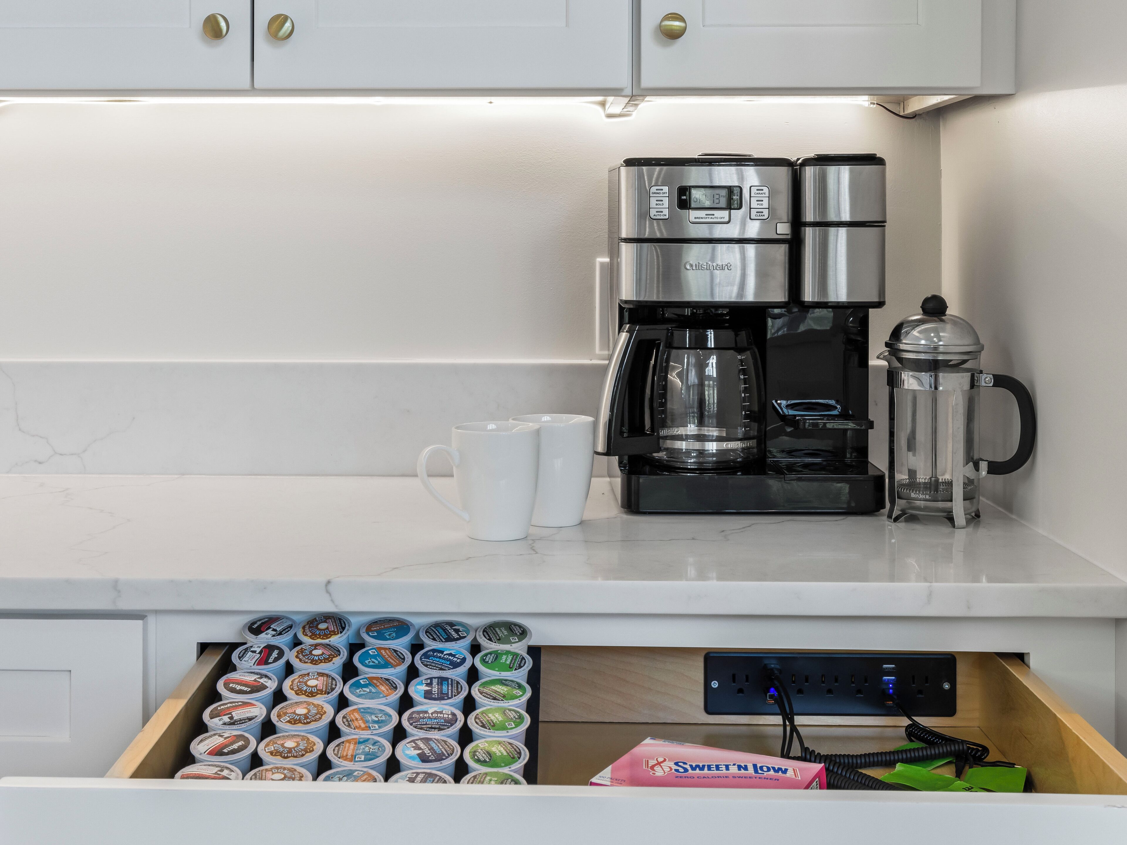 Een keuken met een koffiezetapparaat, een cafetière en een lade vol koffiepads.