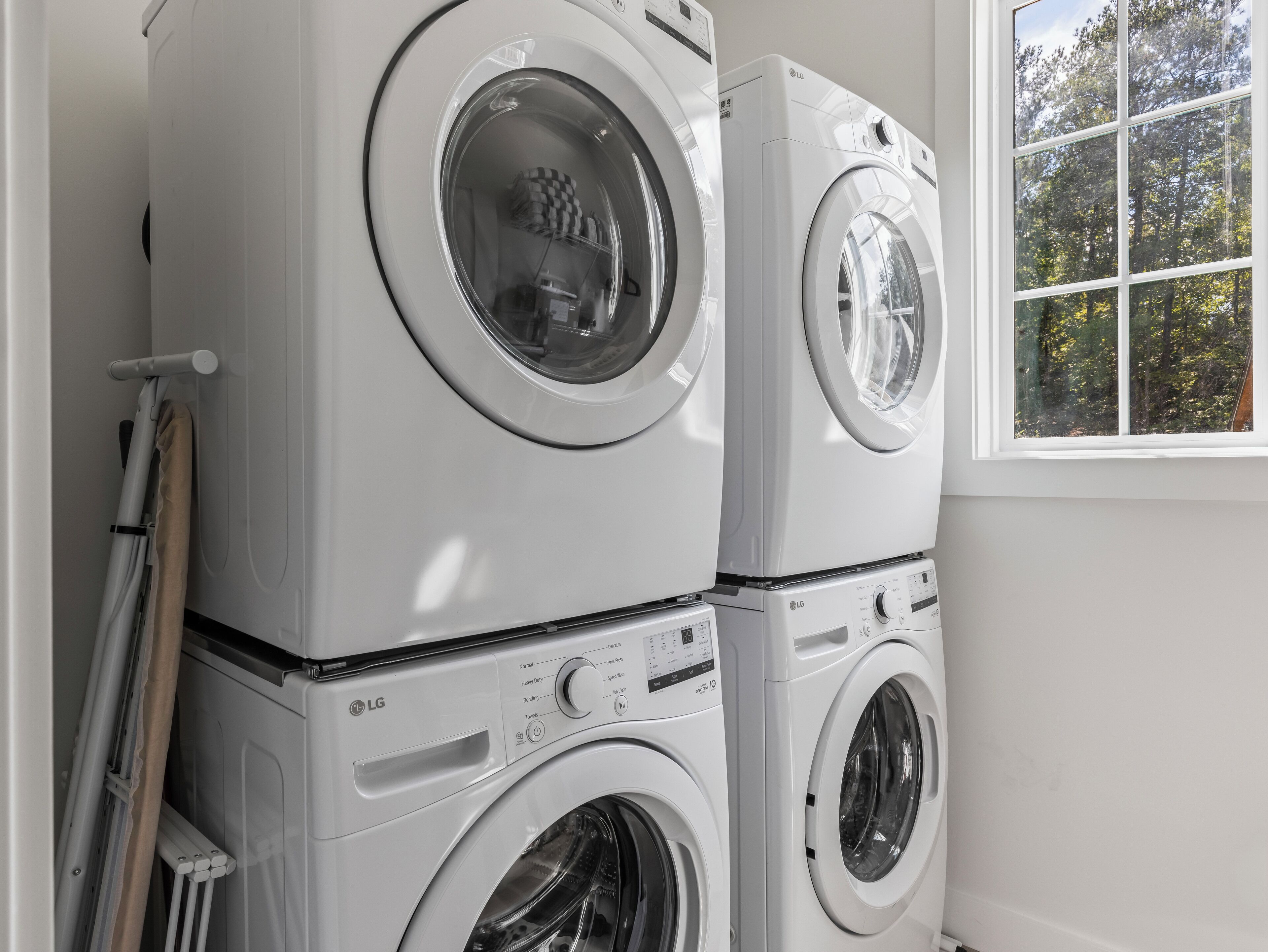 A stacked washer and dryer unit in a laundry room with a window showing trees outside.